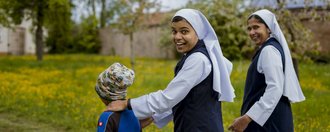 Schloss Hochaltingen Zwei Ordensschwestern gehen mit einem Jungen im Park spazieren und schauen über die Schulter in die Kamera.