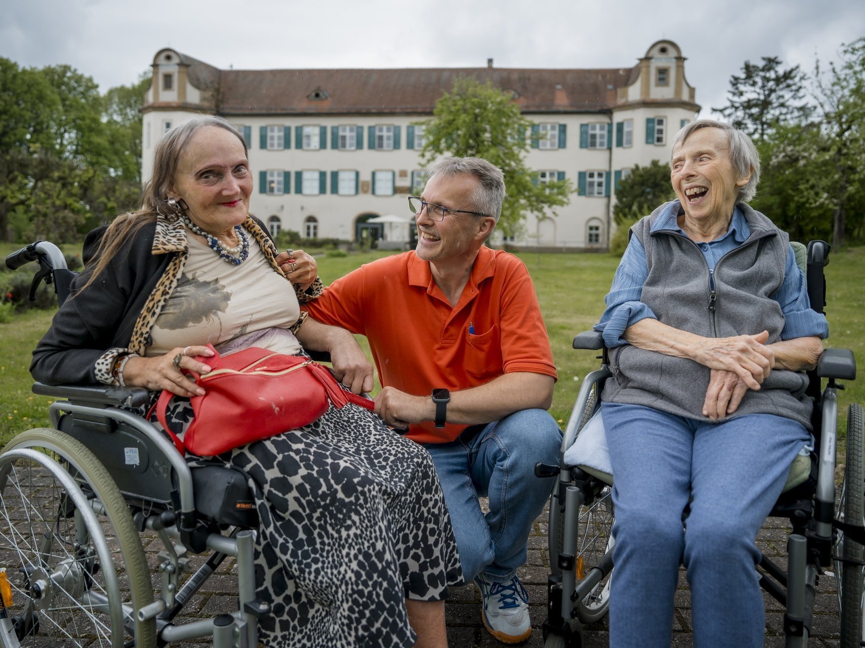 Ein Mitarbeiter sitzt mit zwei Bewohnerinnen im Garten.